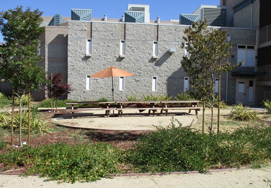 View of a courtyard at James Ranch with picnic tables, an umbrella and a building in the back